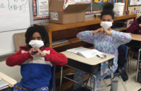 Students at Adams Elementary School wears their new face mask and holds their hands in the shape of a heart to express their gratitude.