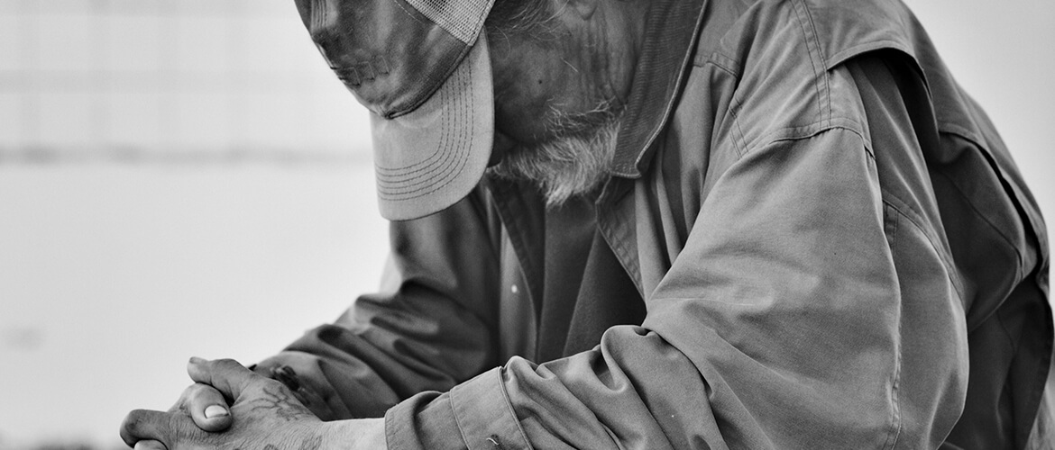 A homeless man sits with his head bowed.