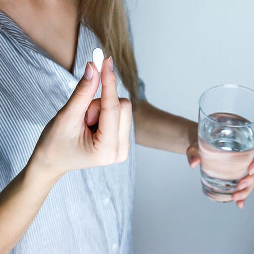 A woman holds her prescription medication and a glass of water.