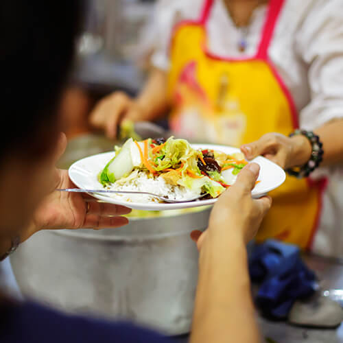 A volunteer serves meals at a homeless shelter.