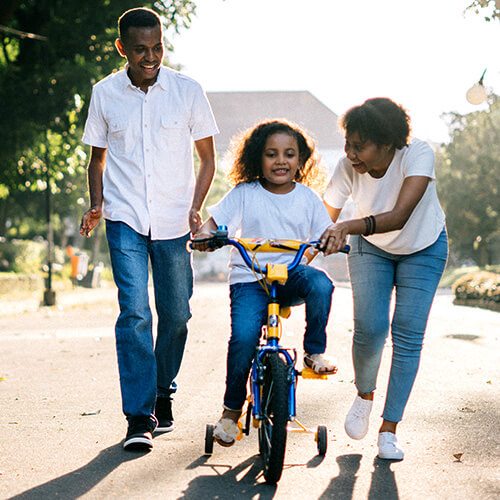 Young family teaching their daughter to ride a bike.