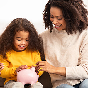 A mom sits on a couch with her daughter and talks with her about the importance of saving money. 